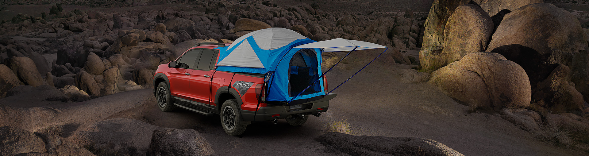 A Honda Ridgeline parked at a camp site with an in-bed tent accessory attached.