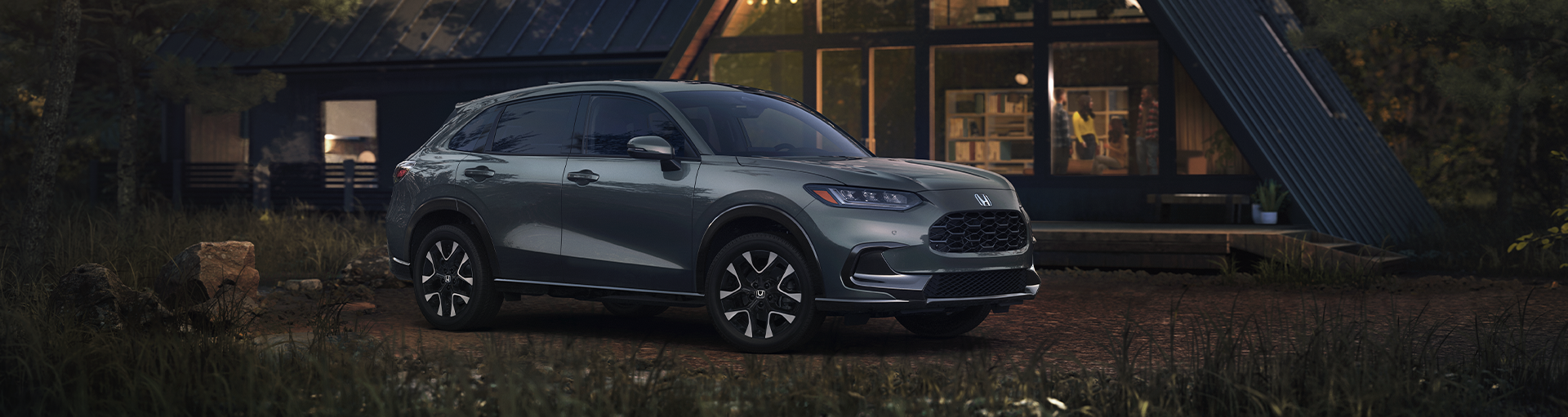 A silver Honda HR-V parked in front of a modern cabin in the woods at night.