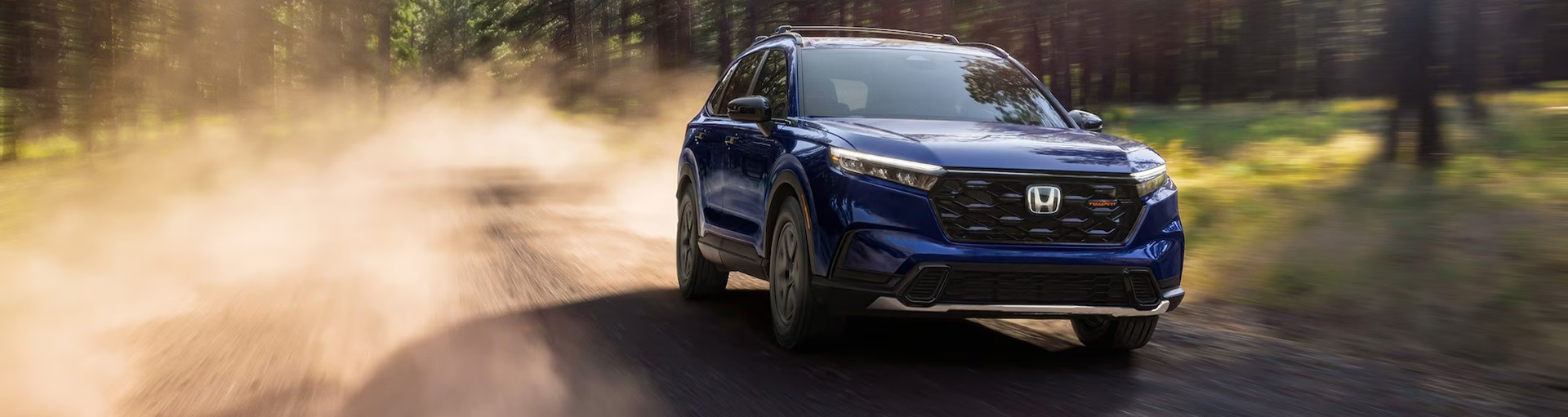 A blue Honda CR-V Hybrid TrailSport leaving a trail of dust driving on a dirt road.